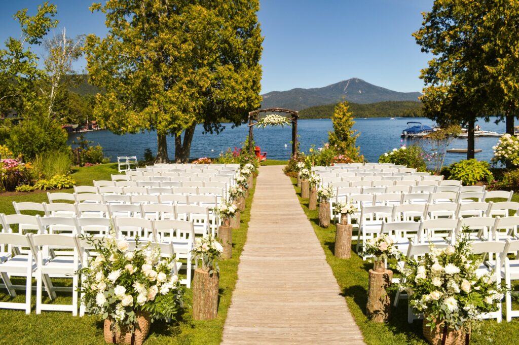 Outdoor wedding venue next to lake with white folding chairs.