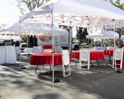 Outdoor canopy tents with round tables, red and white tablecloths, and white folding chairs set up for a 4th of July event in Los Angeles.