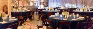 Elegant party event setup with round tables, floral centerpieces, and glassware in a decorated venue. holiday table
