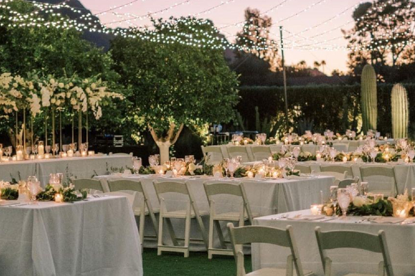 Elegant outdoor wedding reception setup with white chairs, candlelit tables, floral centerpieces, and string lights—available with party event equipment rentals and delivery in Los Angeles.