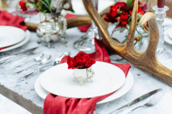 Elegant party table setup with red floral arrangements, deer-top centerpiece, and polished tableware—ideal for event setup and party equipment rentals in Los Angeles.