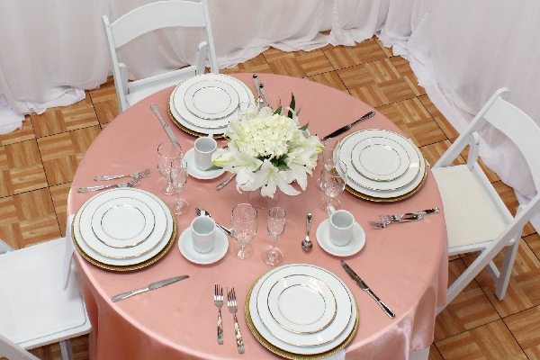 Elegant round table setup with white chairs, gold-rimmed china, glassware, and blush pink linen – party event equipment rentals and delivery in Los Angeles.